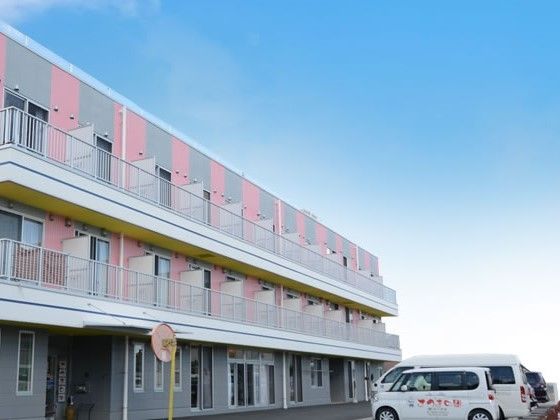 駐車場を併設した、灰色とピンクの外壁の３階建ての施設