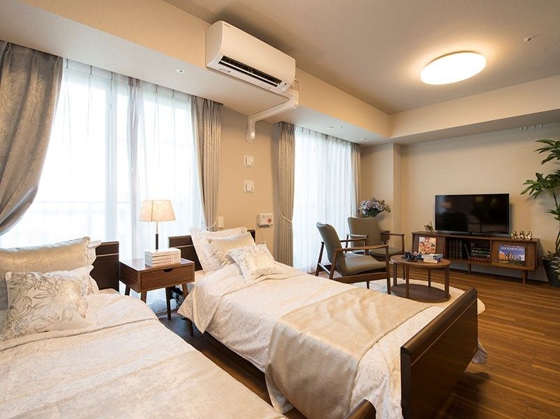 大きな窓が2つ並び、ベッドやテーブルセット、テレビなどが配置された2人部屋