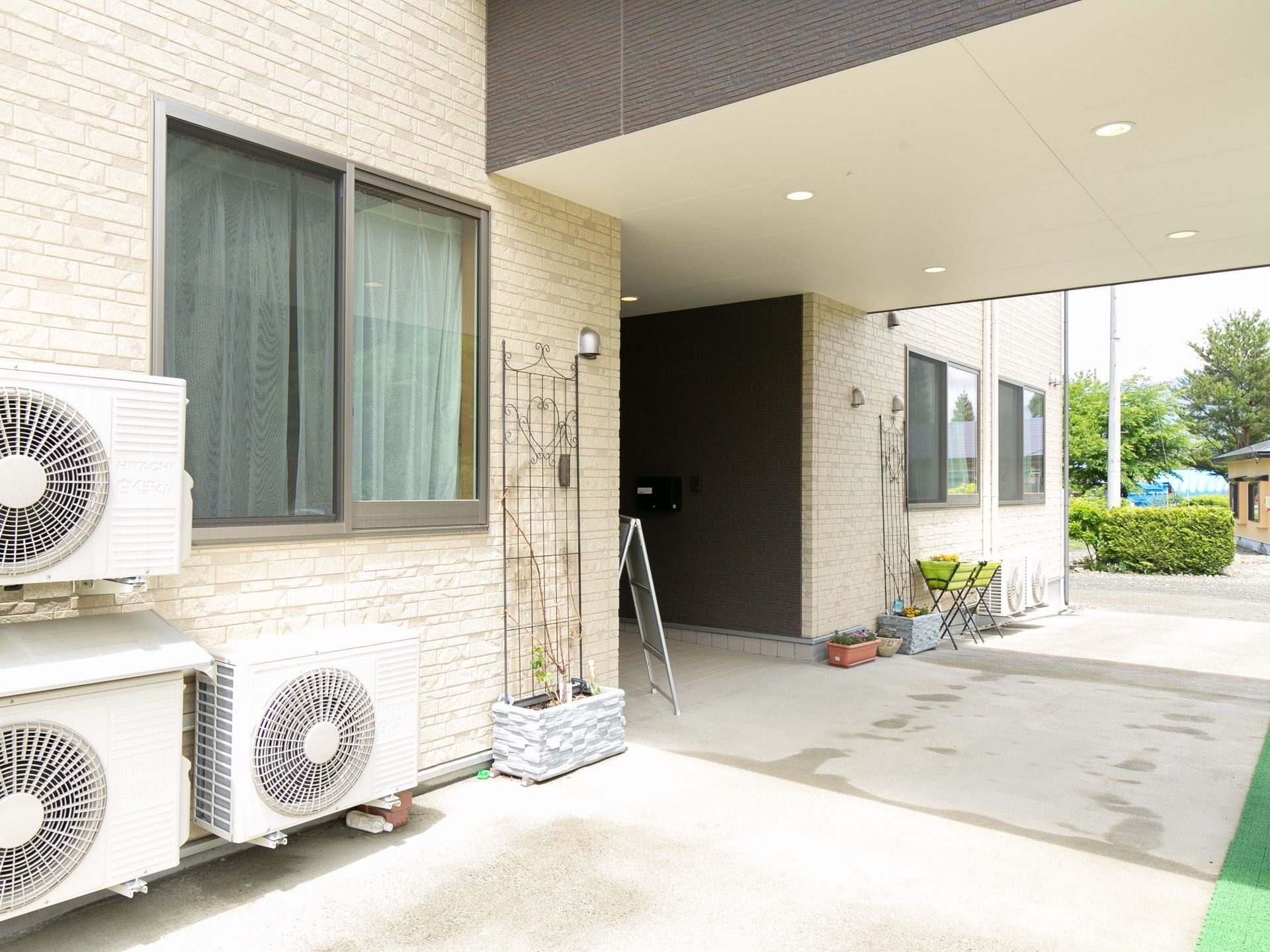 玄関の左右両側の壁沿いにさまざまな形や大きさのプランターが置かれており、色あざやかな植物が育てられている。