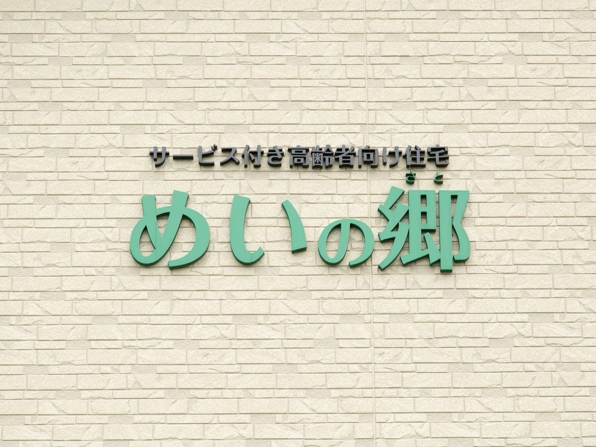 ベージュ色の外壁に施設名が表示されている。緑色の読みやすい大きな文字で書かれており、わかりやすくなっている。