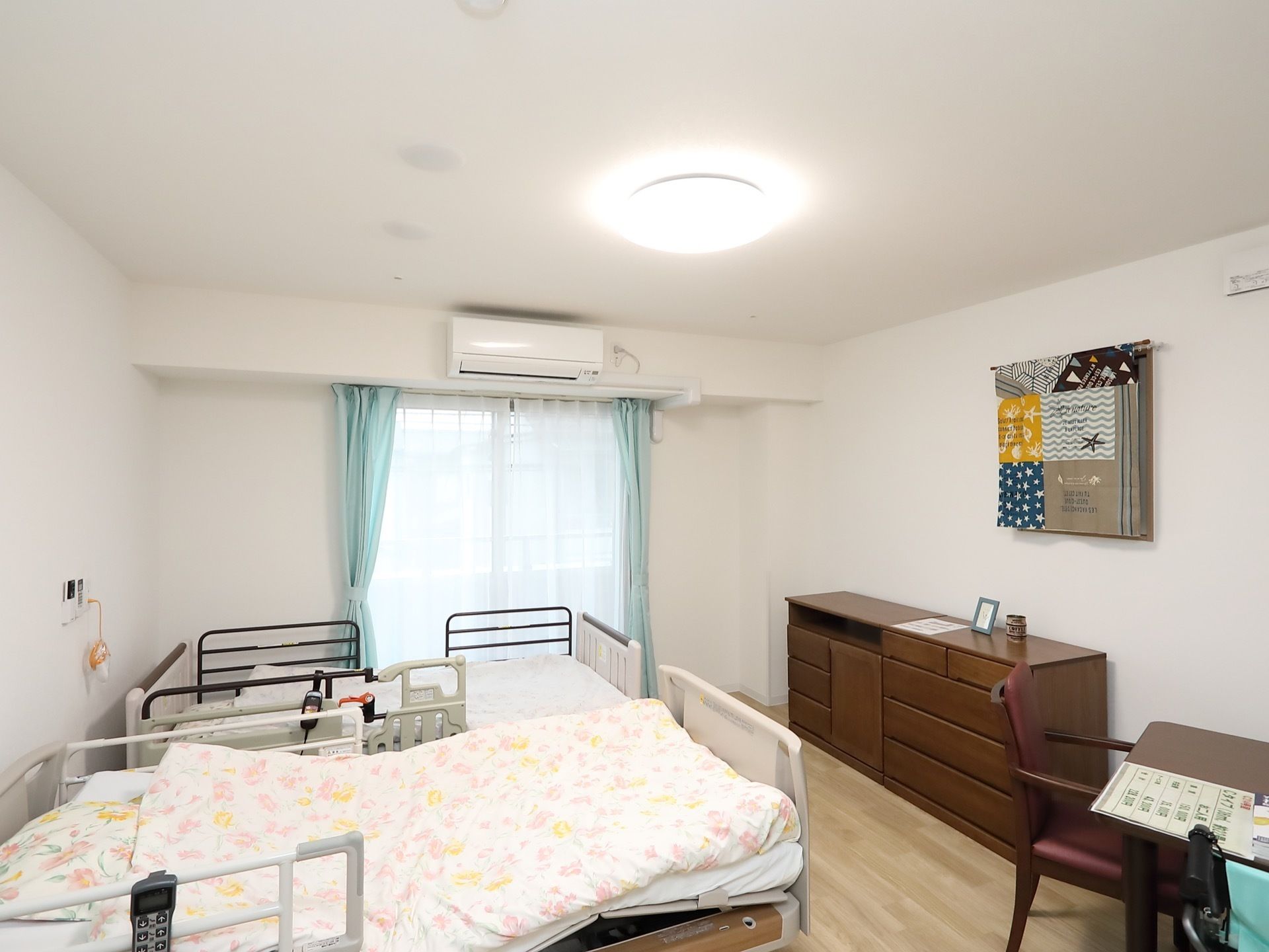 電動ベッドが2台並んでおり、それぞれのベッド柵に操作リモコンが掛けられている。2つのベッドの間の壁にナースコールが取りつけられている。