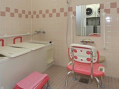 薄いピンク色を基調とした室内で、シャワーチェアー、バスボード、浴槽台が設置されている。シャワー脇には、手すりも付いている。