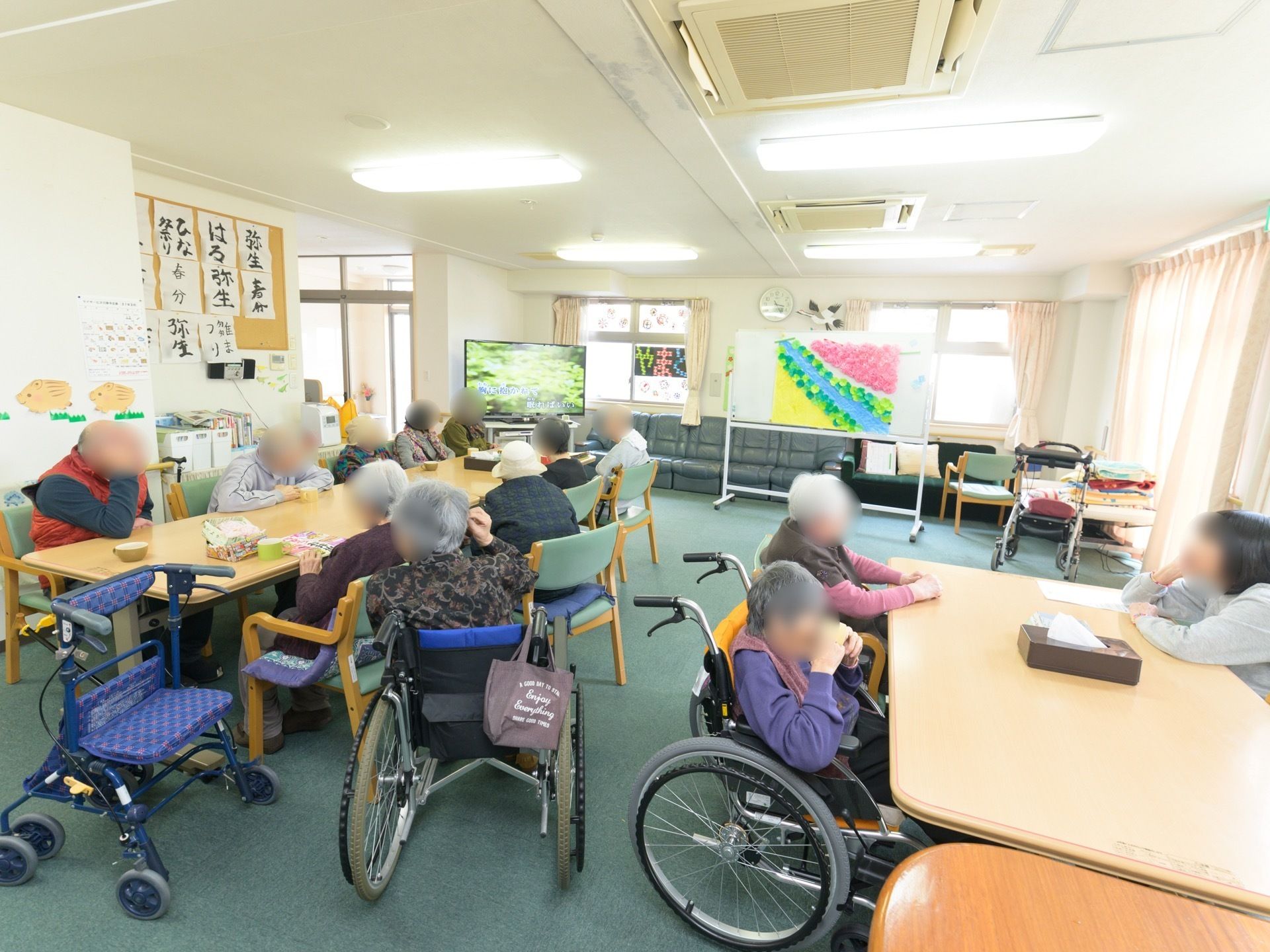 共有スペースに多くの入居者様が集まっている。テレビを見たり、スタッフと話をしたり、お茶を飲んだりしている。