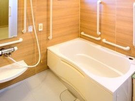 ウッド調の壁にいくつも手すりが取り付けられた、ナースコール完備の浴室