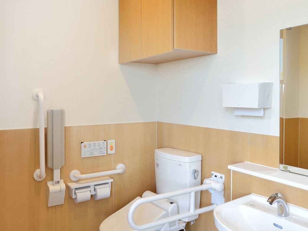 温水洗浄付き暖房便座トイレがあり、周りには手すりが取り付けられている。ナースコールが設置してあり、上部には収納棚がある。