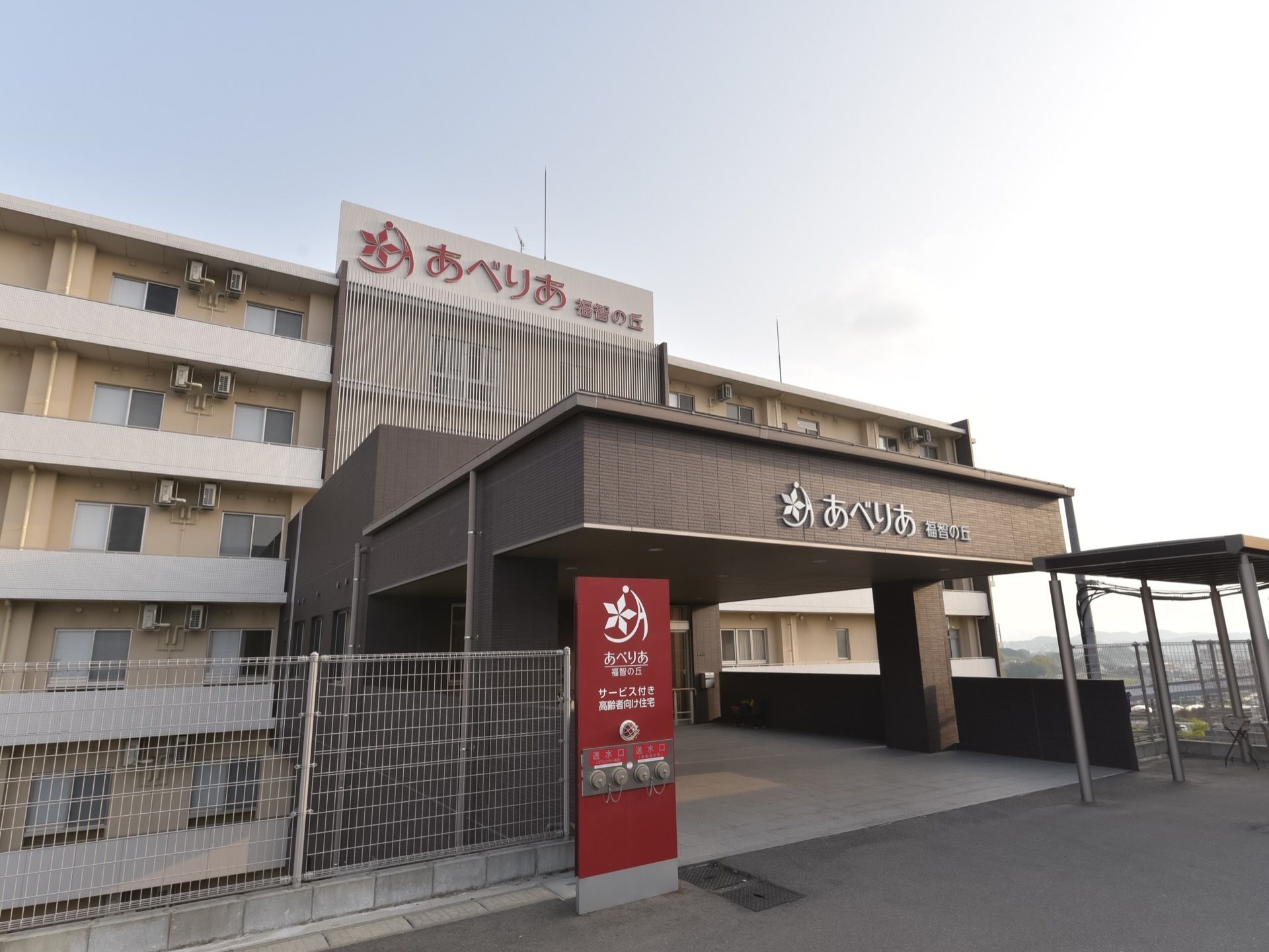 玄関は建物の上層階に繋がっている。入口の幅が大変広く取られている。建物の屋上に大きく施設名が表示されている。