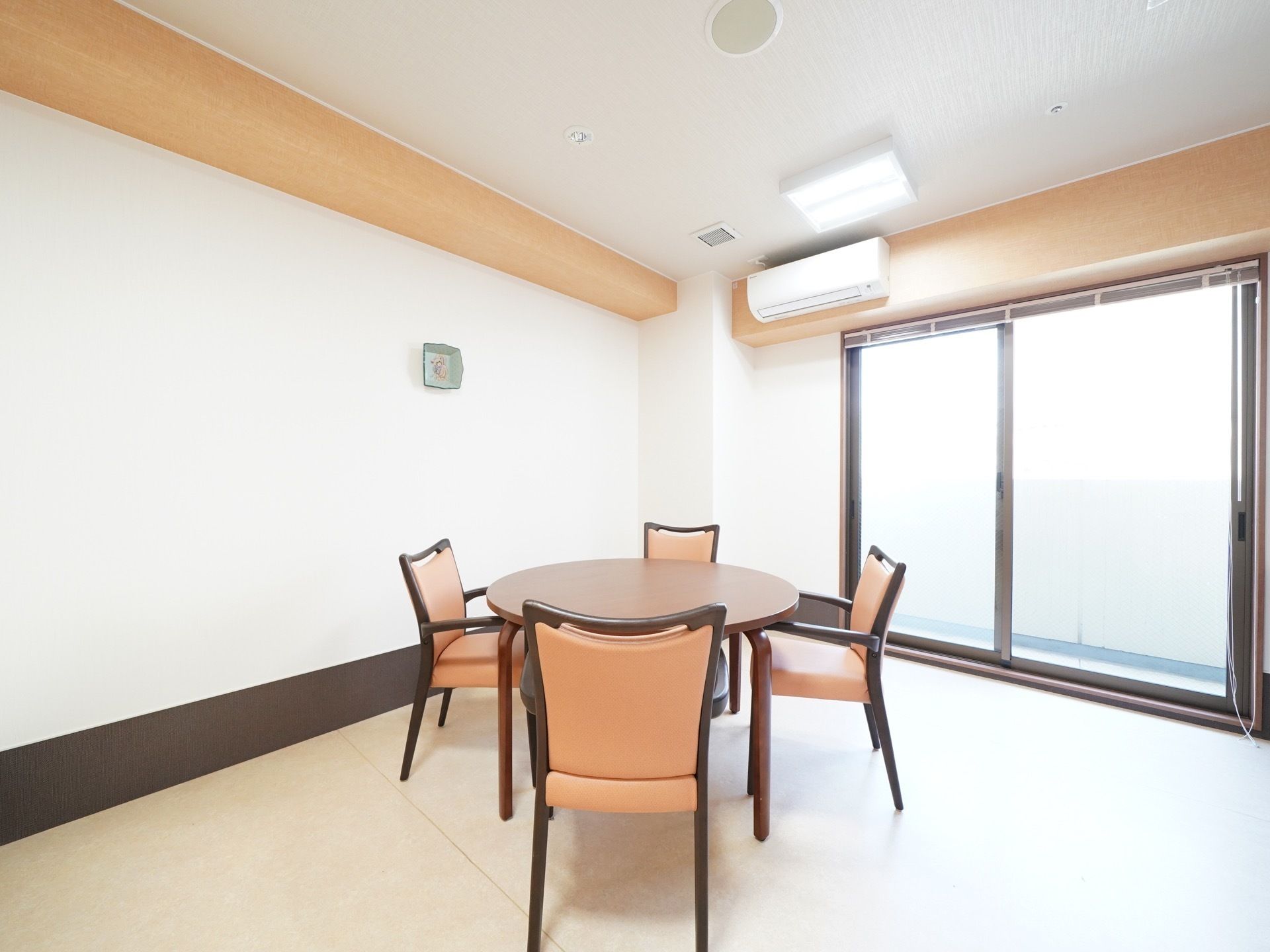 大きな窓から光が多く差し込んでいる部屋である。白とベージュが使われ清潔感が漂っている。中央には丸テーブルと椅子が4脚置かれている。