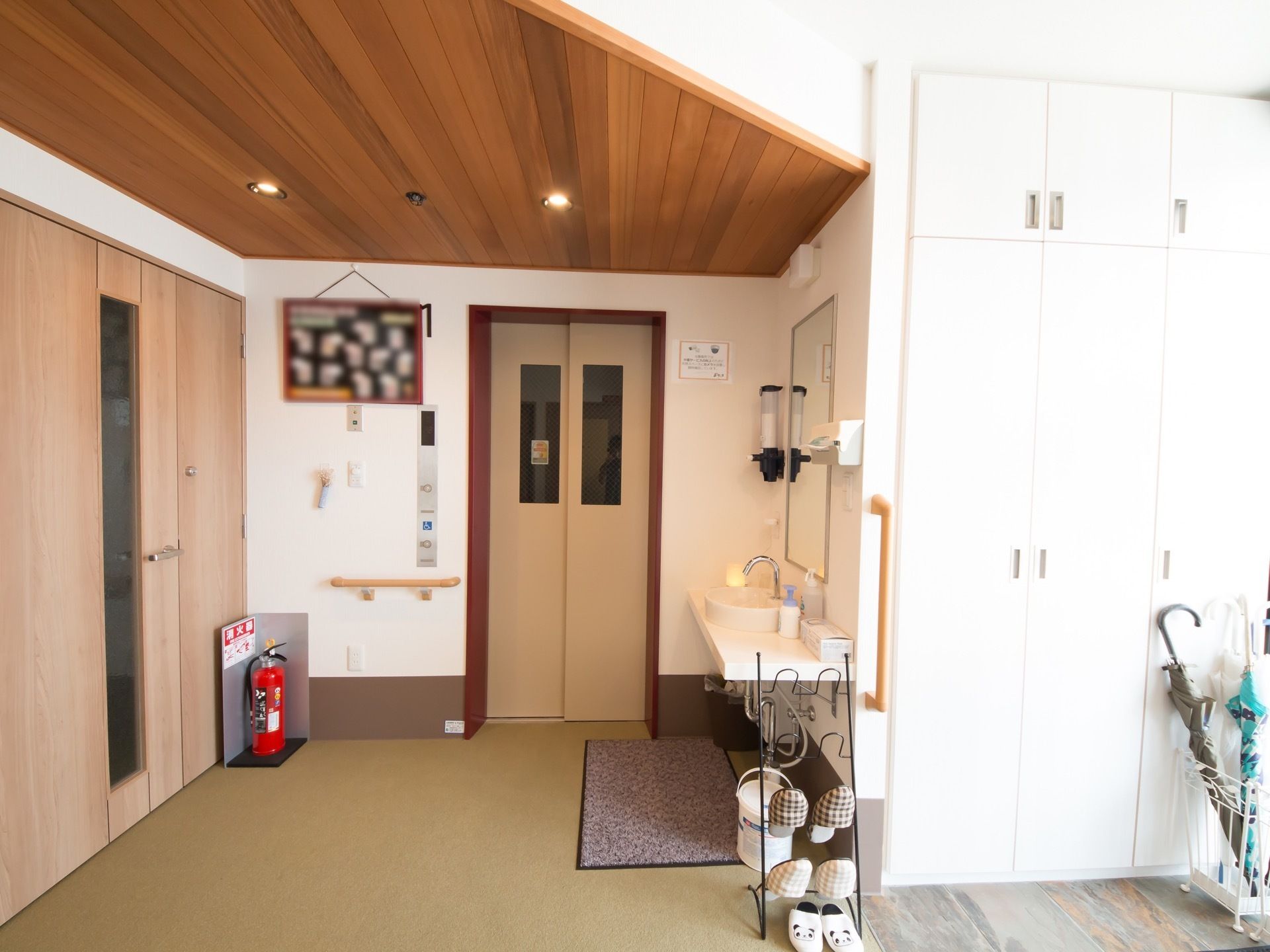 傘立てに傘が建てられ、スリッパラックに２足のスリッパが掛けられている。車椅子対応の洗面台が設置されている。