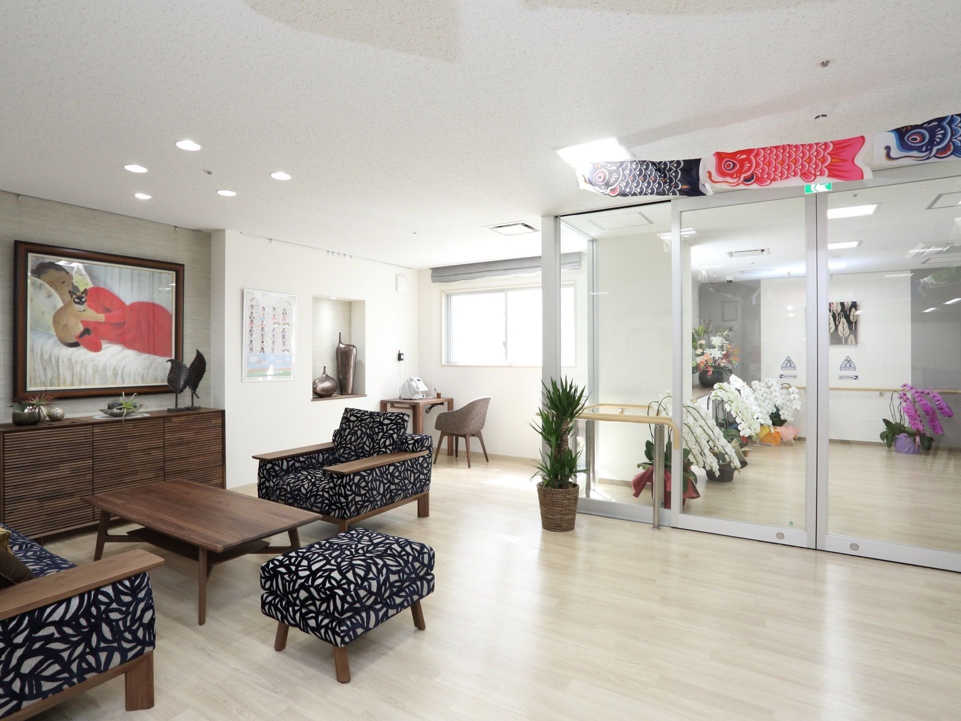 明るい空間に絵画やソファが設置されている。部屋の仕切りには自動ドアが設置されていて、沢山の胡蝶蘭がガラス越しに見えている。