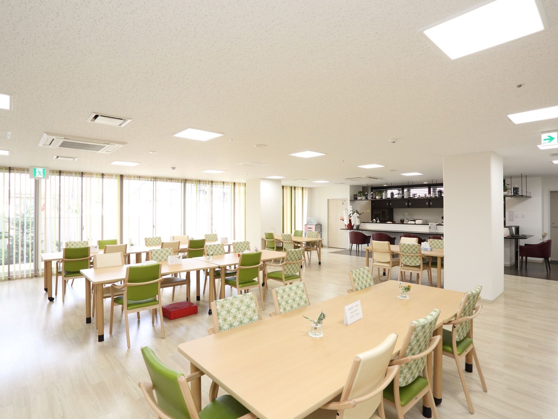 大きな窓が数多く設置されている。テーブルや椅子が並んでいる。一角にカウンターが設置されていて、その前に椅子が置かれている。