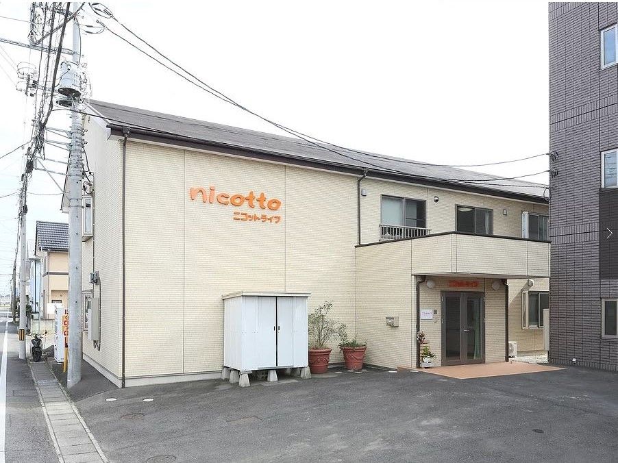 玄関周りに観葉植物や倉庫が置かれた、2階建ての建物