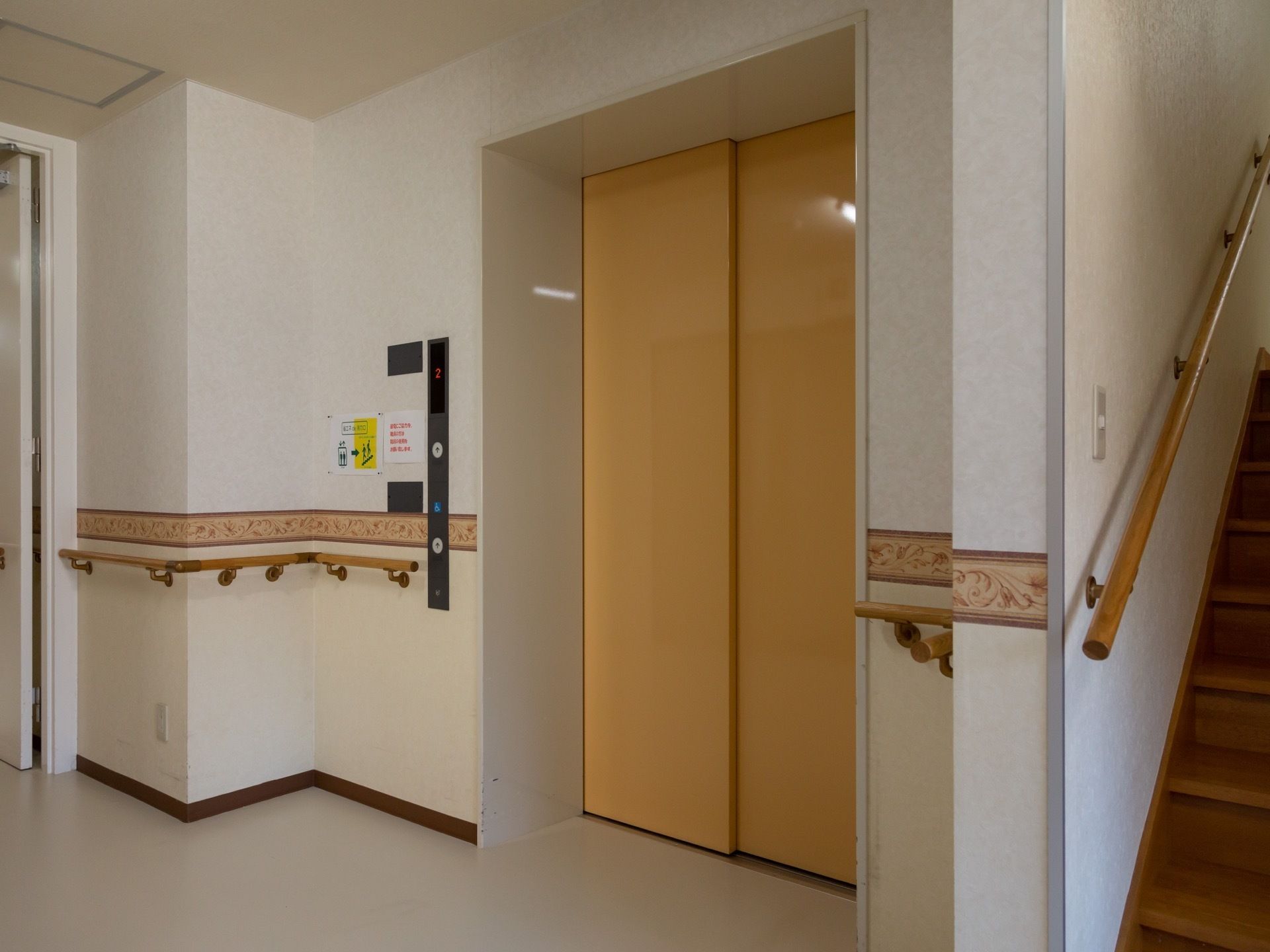 茶色い扉のエレベーターがあり、その右側に階段がある。扉の横の壁に呼び出し用のボタンが２か所に設置されている。