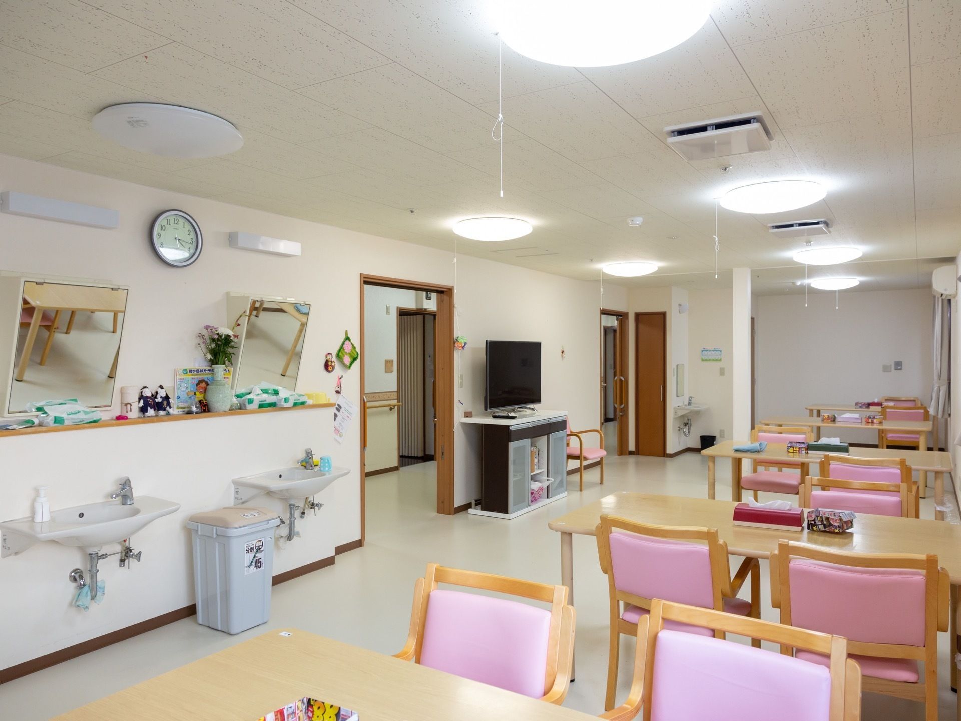 共有スペースの左奥には洗面台が２か所にある。４人用のテーブルセットが並び、ピンクの椅子が並べられている。