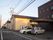 オレンジの外壁で三角の屋根が乗った建物と、３階建ての建物で構成されている。施設前は駐車スペースがあり、自動車が停められている。