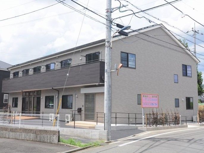 低い柵で囲まれた、落ち着いた茶色の外壁の2階建ての建物
