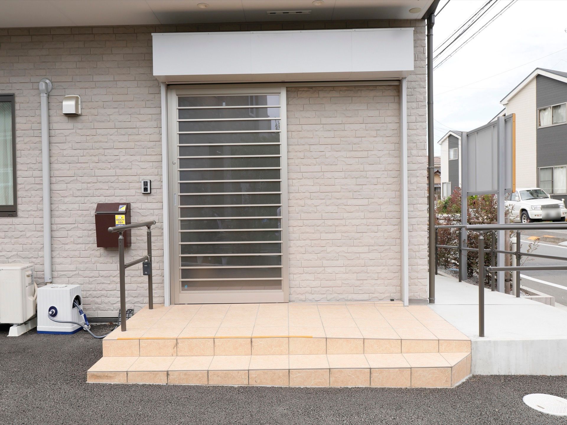 グレーのスタイリッシュな扉が備え付けられている。となりにはインターホン、ポストがある。手すりも完備されている。