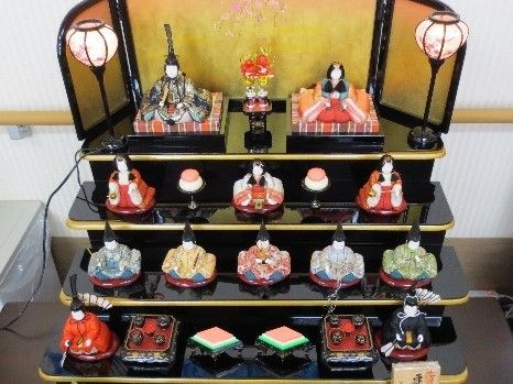 ひな壇の頂上に座るお内裏様・お雛様の間には、桃の花が優美に飾られている。ぼんぼりは電化式であり、火を使う心配がない。
