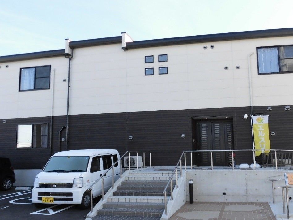 施設名が表記された看板を取り付けている。入口までは手すり付きスロープと階段を設置し、出入りしやすくしている。