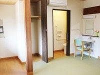トイレのドアが開いている部屋。その上にはエアコンが設置されている。横に椅子があり、下にはカーペットが敷かれている。