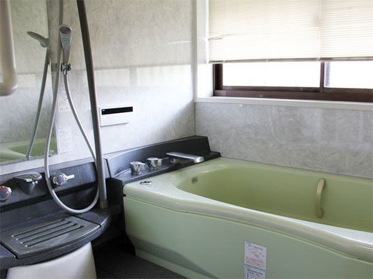 浴槽の中とシャワーの横に手すりが設置された浴室。壁には大きな窓があり、目隠しも兼ねたブラインドを掛けている。