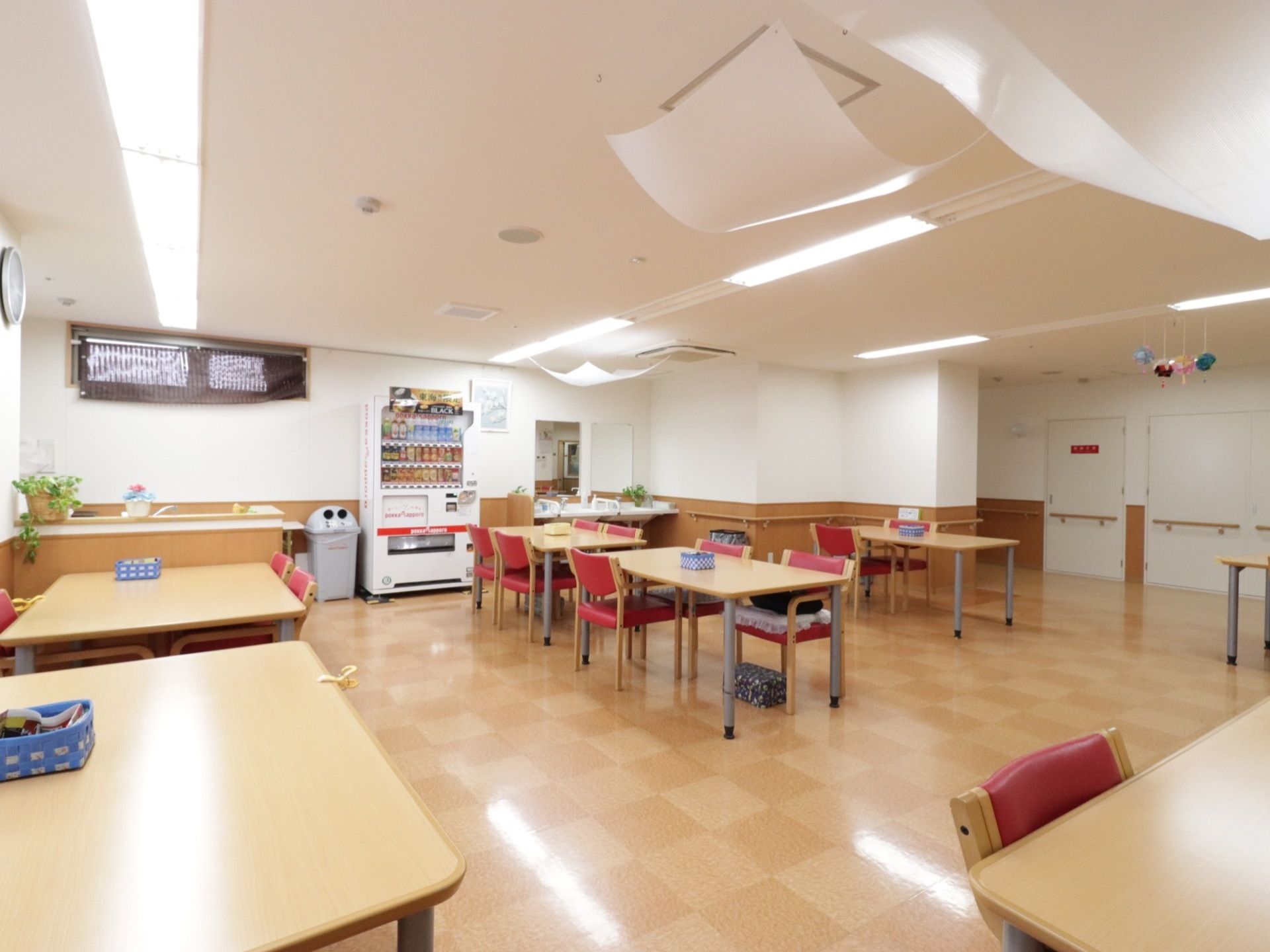 壁側に自動販売機とゴミ箱がある。テーブルと椅子は間隔をあけて配置され、机の上には小さな籠状のクズ入れがある。