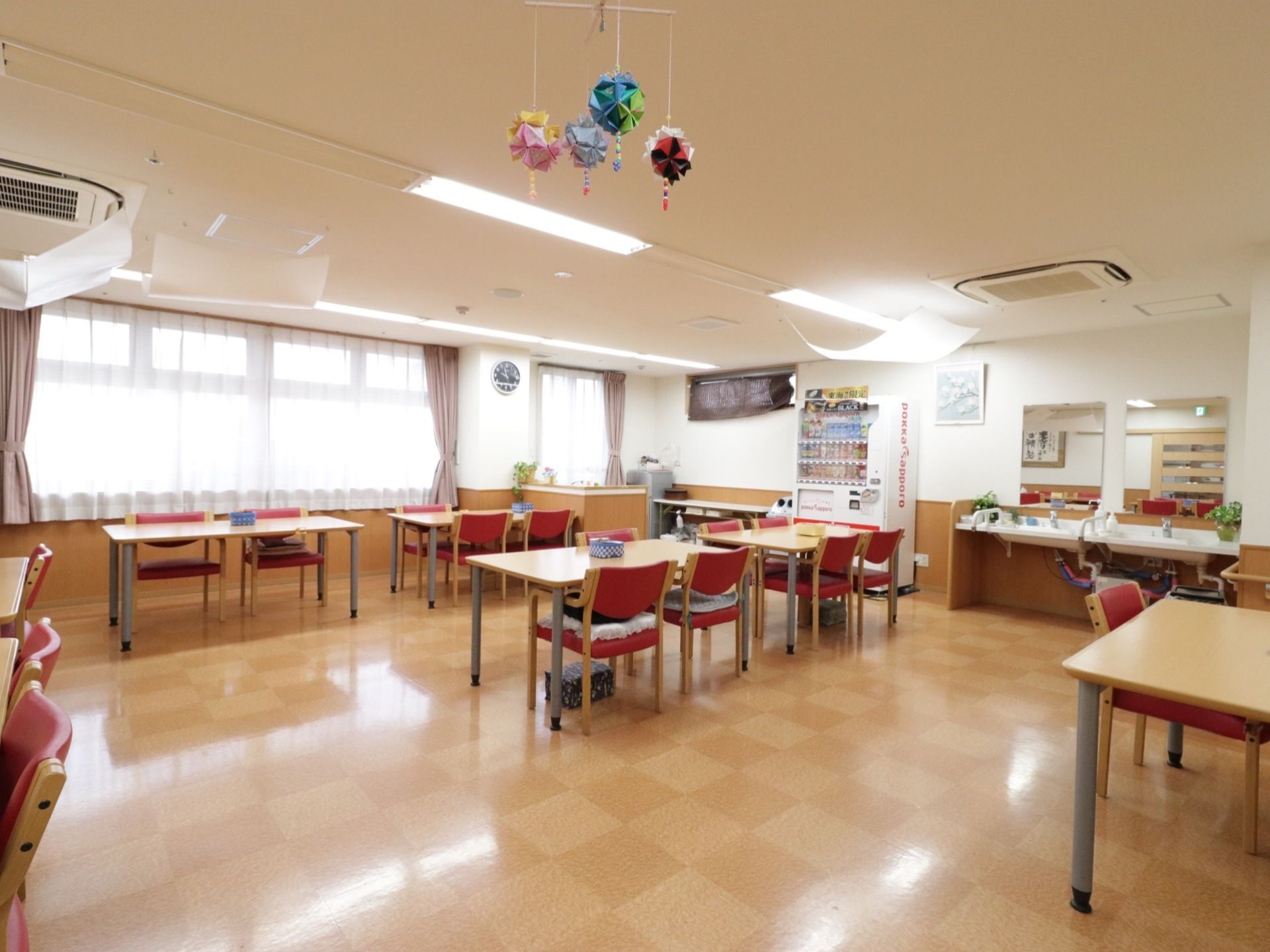 壁一面に窓があり明るい。部屋の隅には洗面台と鏡が設置されている。隣には自動販売機もある。天井には手作りの飾りが吊るされている。
