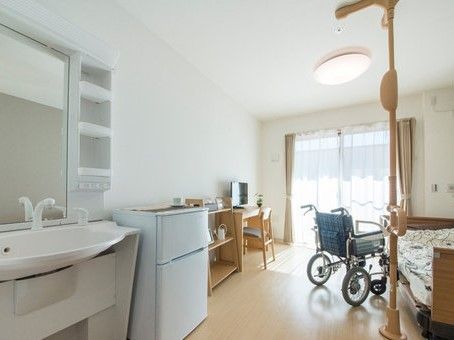 車椅子や介護ベッド、冷蔵庫、家具が並んだフローリングの部屋