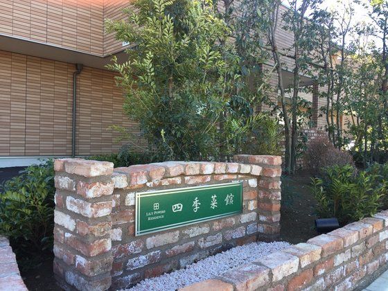 レンガ造りの植え込みの中に設置された、緑色のプレートの施設看板