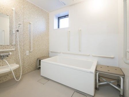 椅子や手すりが複数設置された、明るく清潔感のある浴室
