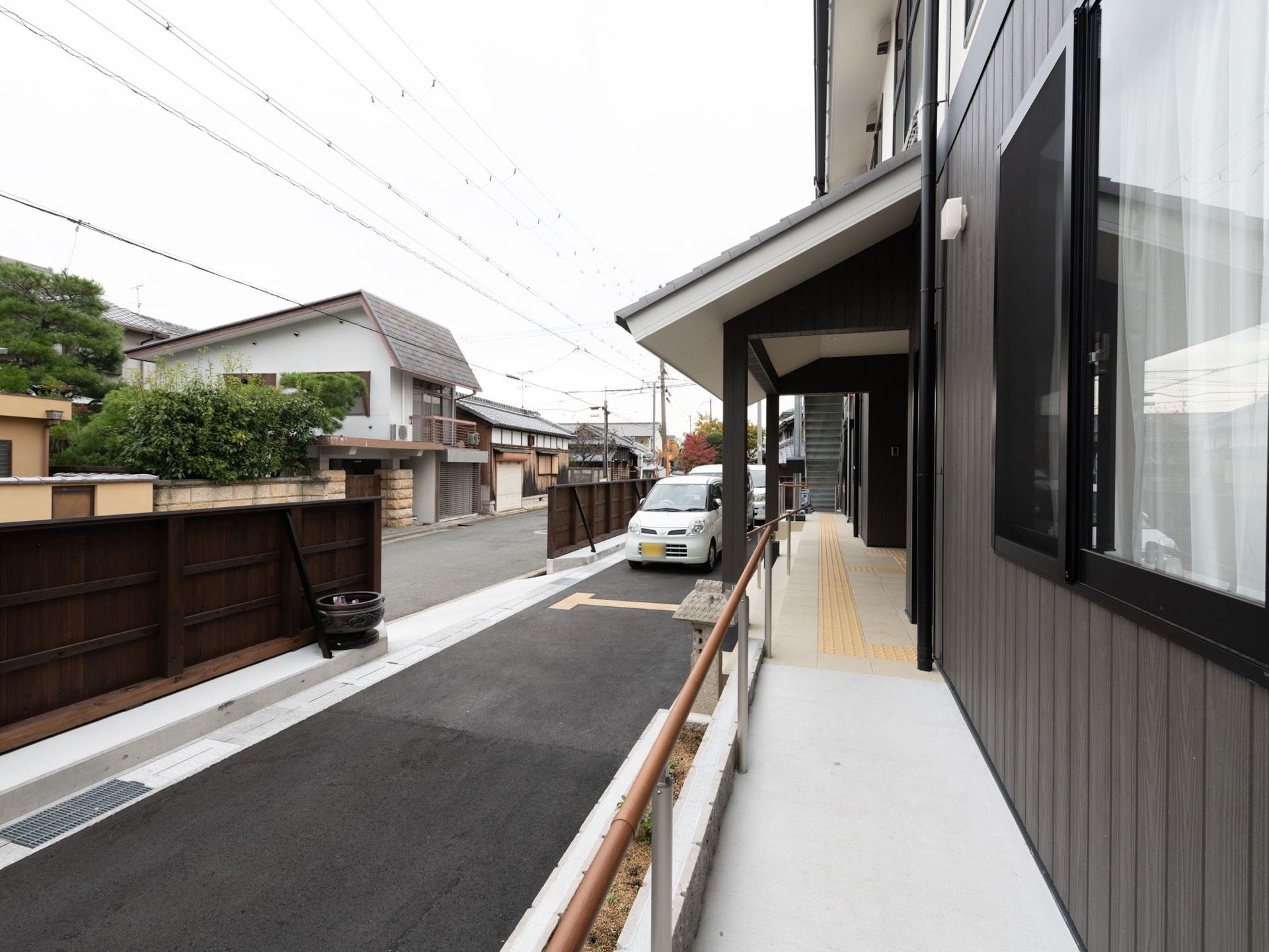 道路と敷地は木の塀で仕切られている。玄関前は車を寄せられるスペースがあり、階段と手すり付きのスロープが設けられている。