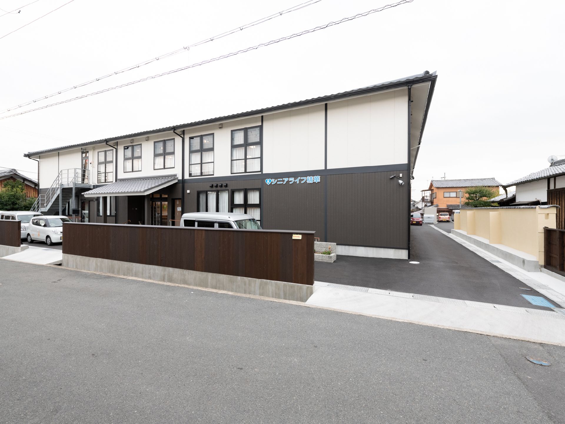 玄関の周りに大きな窓が並び、横に車が停められている2階建ての施設
