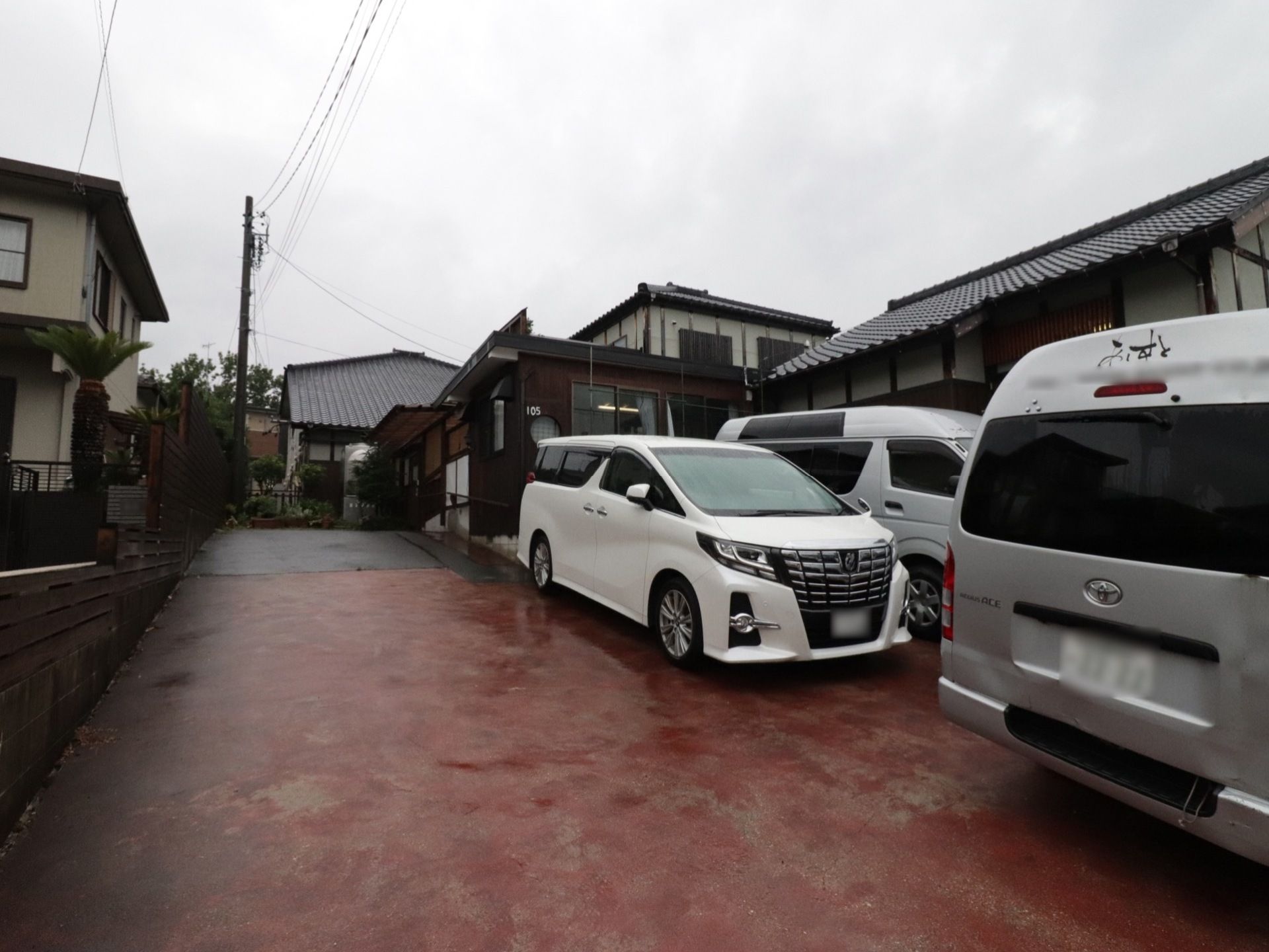 建物の前に赤茶色に舗装された大きな駐車場がある。大型のワンボックス送迎車を３台停めてもまだ余裕の広さである。