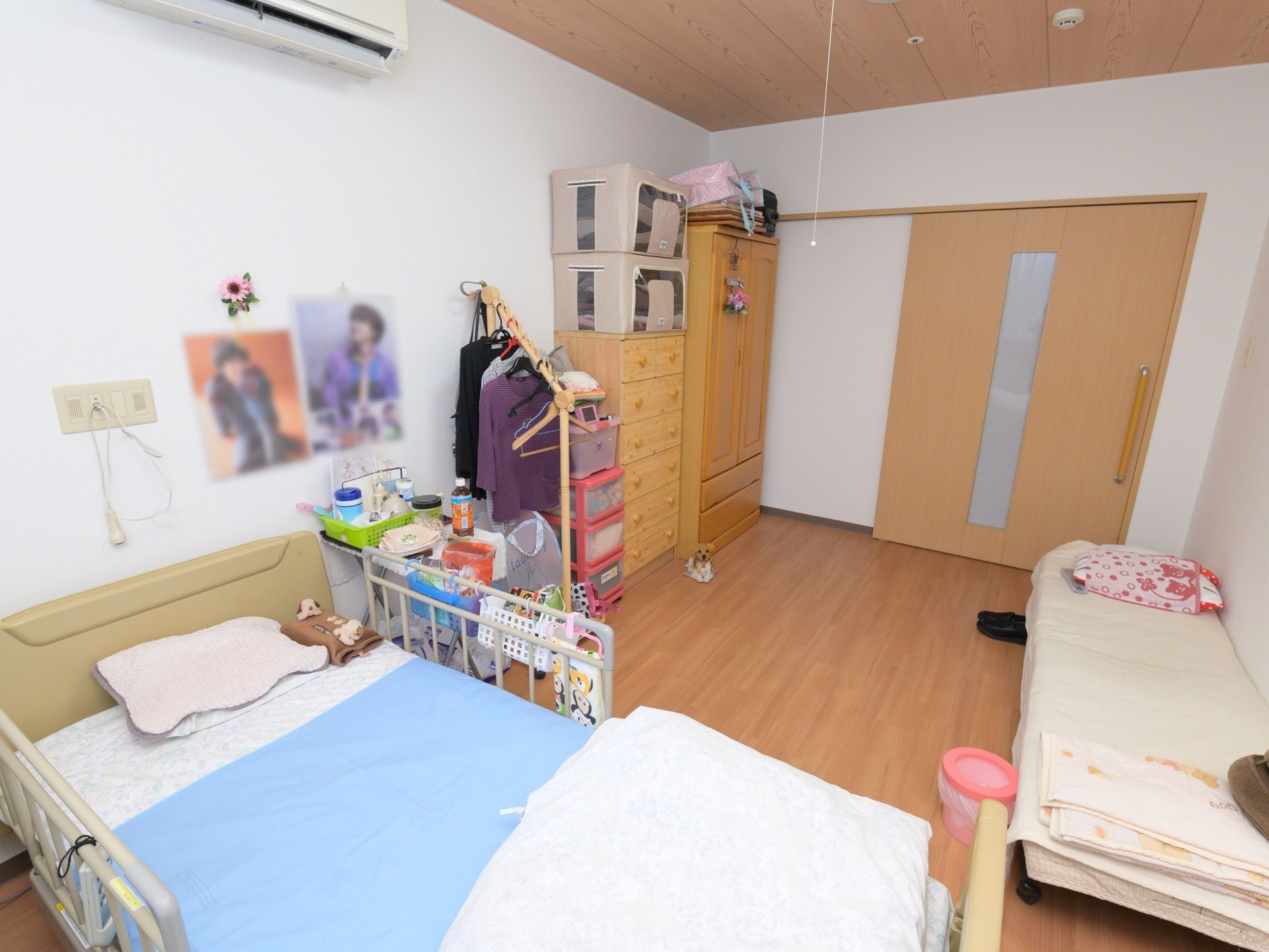 介護用ベッドやタンスが置かれている。広々としたフローリングで段差がない。壁にはポスターが貼られている。
