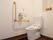 便座ふたのない白い洋式トイレが設置されている。壁に紐がついたナースコールと手すり、ペーパーホルダーが取りつけられている。