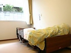 明るい光のさしこむ窓の下に介護ベッドが置かれた、フローリングの部屋