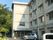 緑に囲まれた施設。4階建ての大きな建物で、玄関先には屋根が付き、車も止まっている。