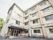 緑豊かな自然に囲まれた、４階建ての施設の外観である。玄関前に椅子とベンチが置かれており、日向ぼっこをお楽しみいただける。