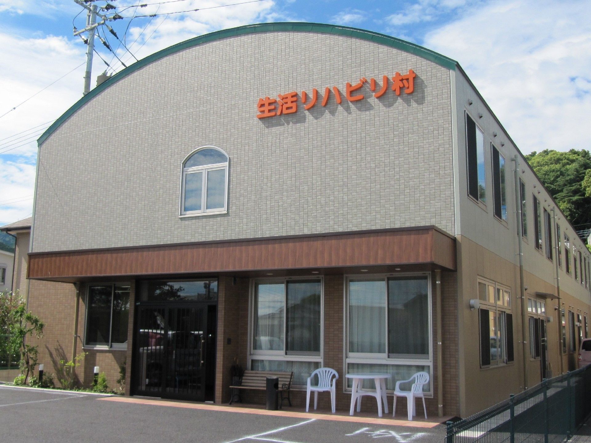 丸い屋根が特徴的な建物。玄関は大きく、車椅子での出入りも楽に行える。生活リハビリ館と大きくオレンジ色の文字で壁に取り付けられている。