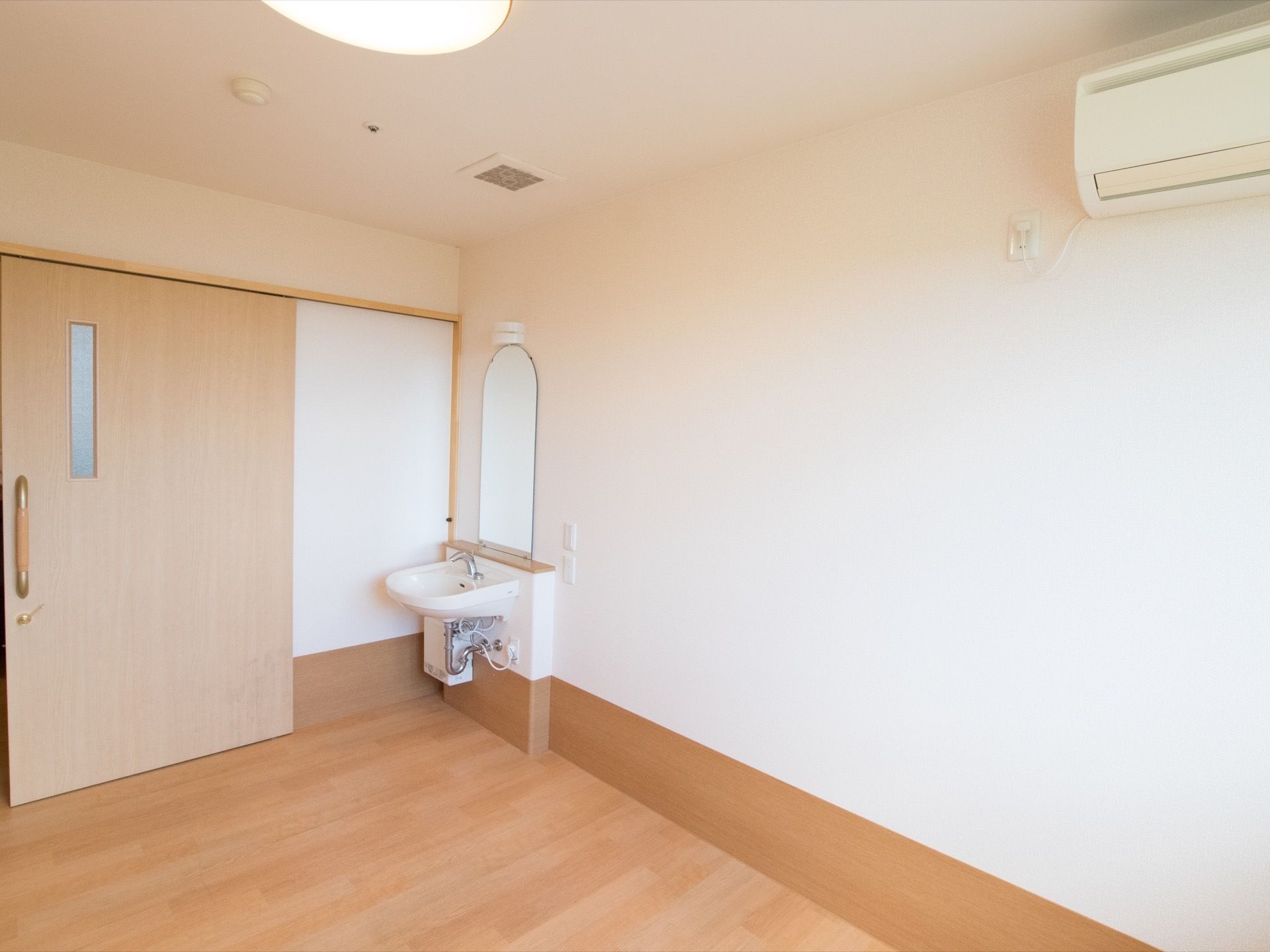 居室のドアは広く開く事ができるスライド式のドアになっている。ドアの近くに鏡のついた洗面台が設置されている。