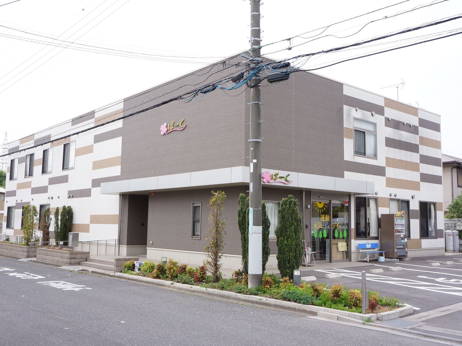 施設の周囲には手入れがされた植栽があり、駐車場が完備されている。自動ドアのそばには自動販売機とベンチが置かれている。