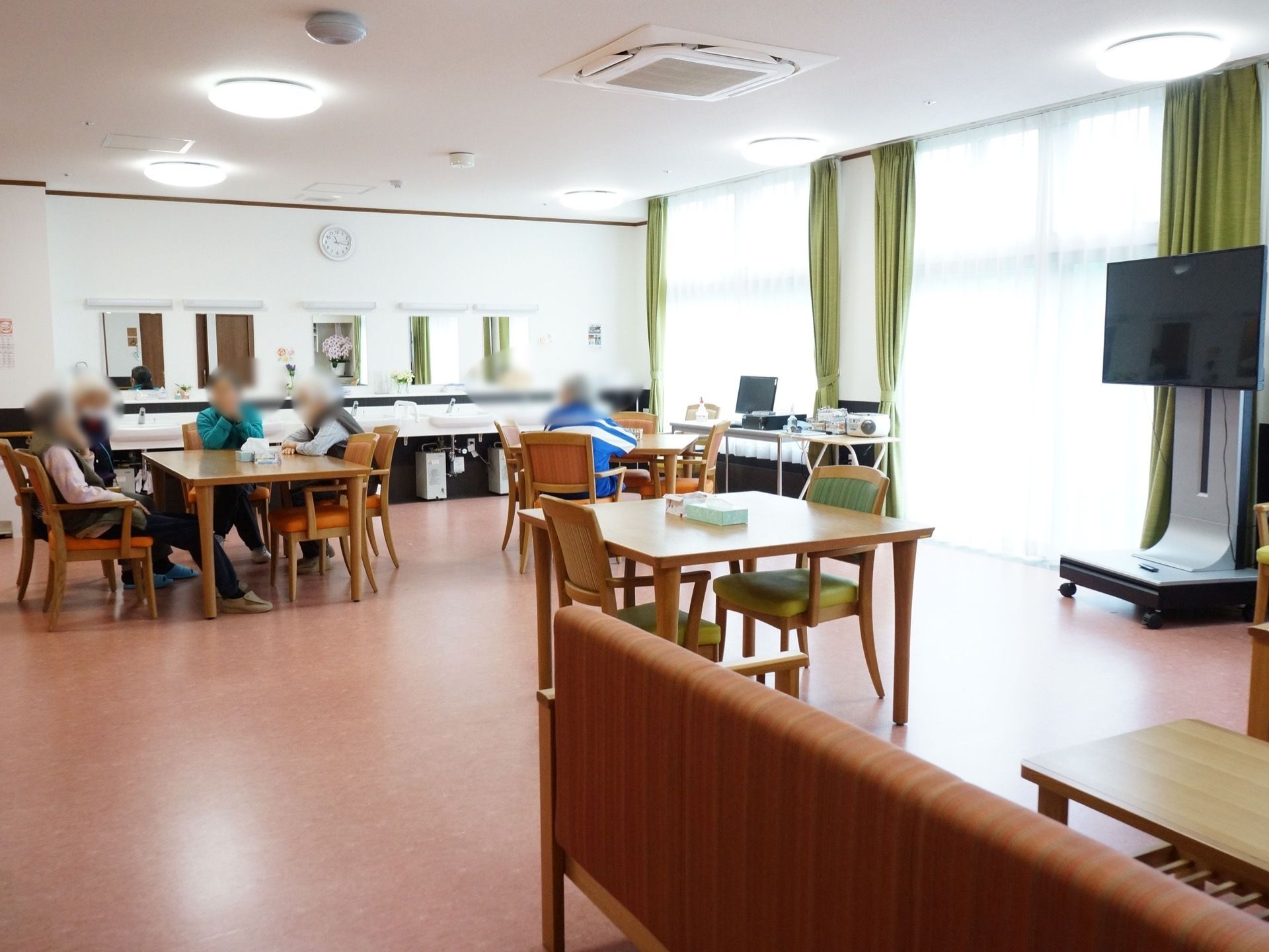 食堂で入居者様が、歓談など思い思いの過ごし方をしている。テーブルの間隔が広く、車椅子や歩行器をご利用の方も移動しやすい。