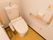 白い壁に囲まれた個室トイレで、便座には温水洗浄便座が取りつけられている。壁には手すりのほか、非常ボタンもある。