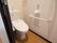 白を基調とした清潔なトイレである。洗浄機能付きの便座が設置されている。壁には手すりとナースコールが取り付けてある。