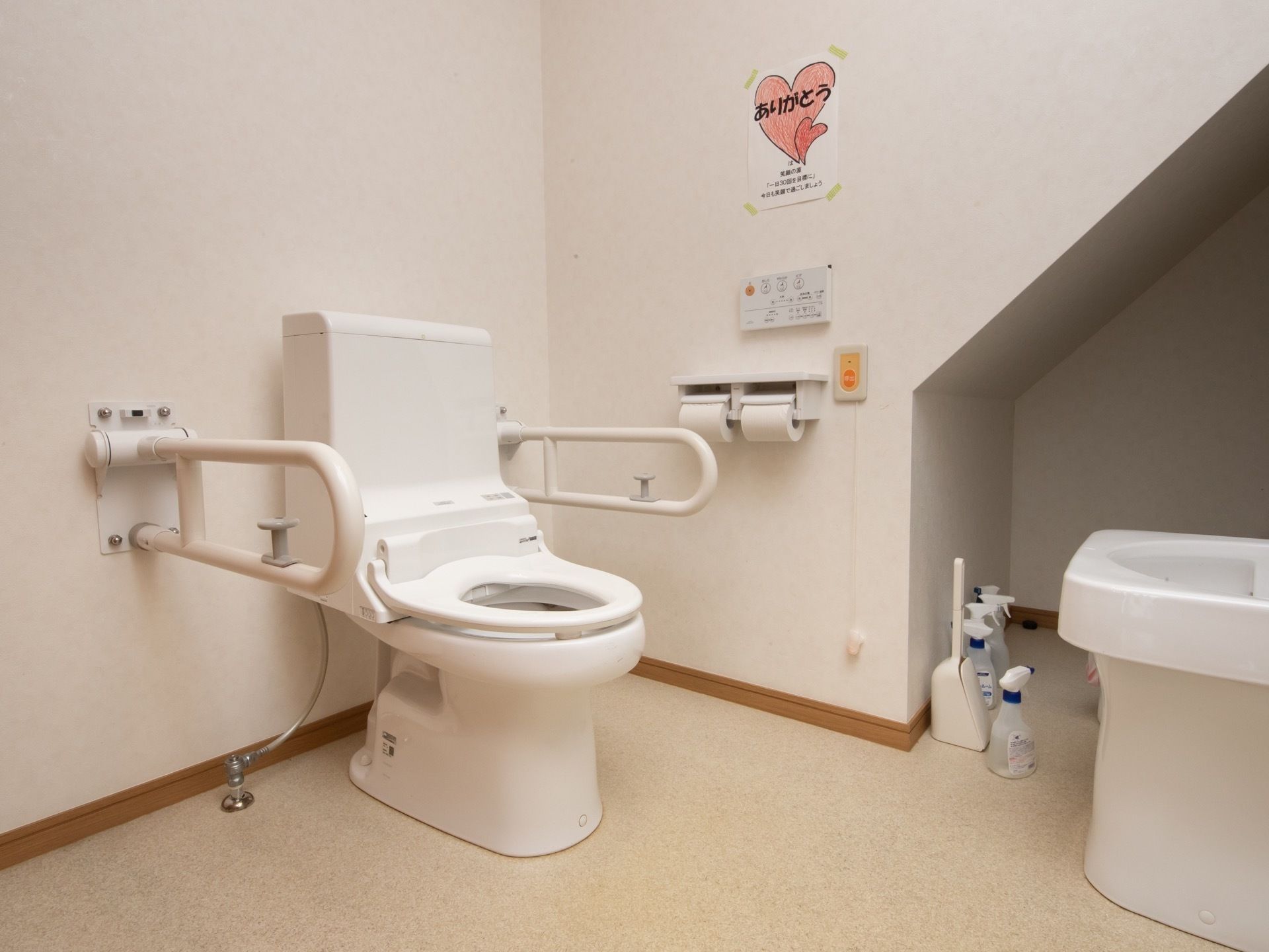 温水洗浄機能付きのトイレが設置され、両サイドに可動式の手すりが取りつけられている。壁にはケアコールも設置されている。