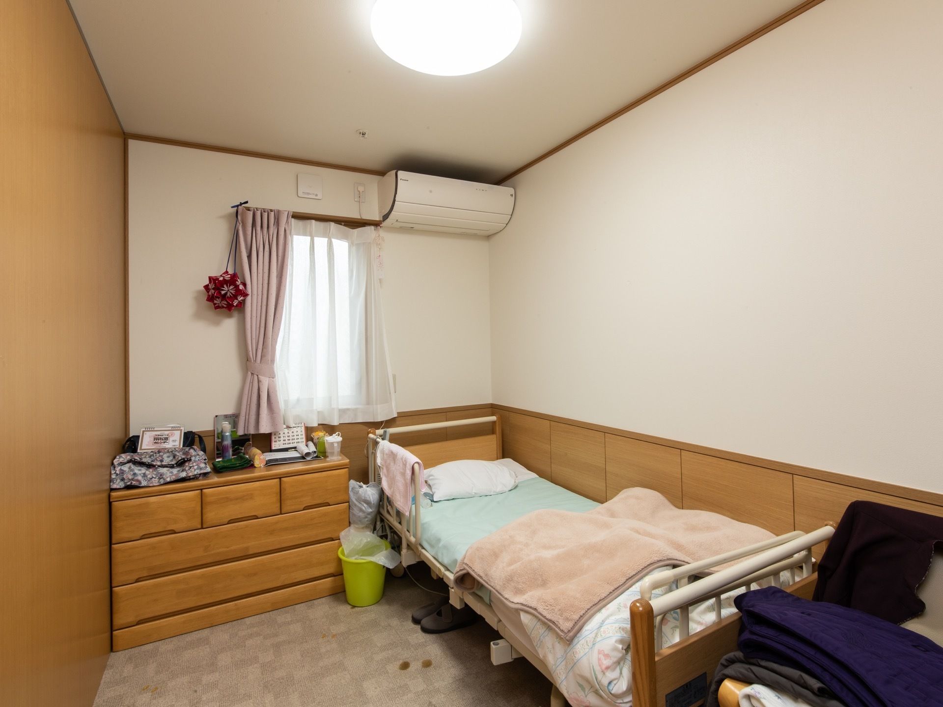 木目調の木板と白い壁に囲まれたシンプルな居室である。ベッドと収納タンスが置かれている。壁にはエアコンも設置されている。