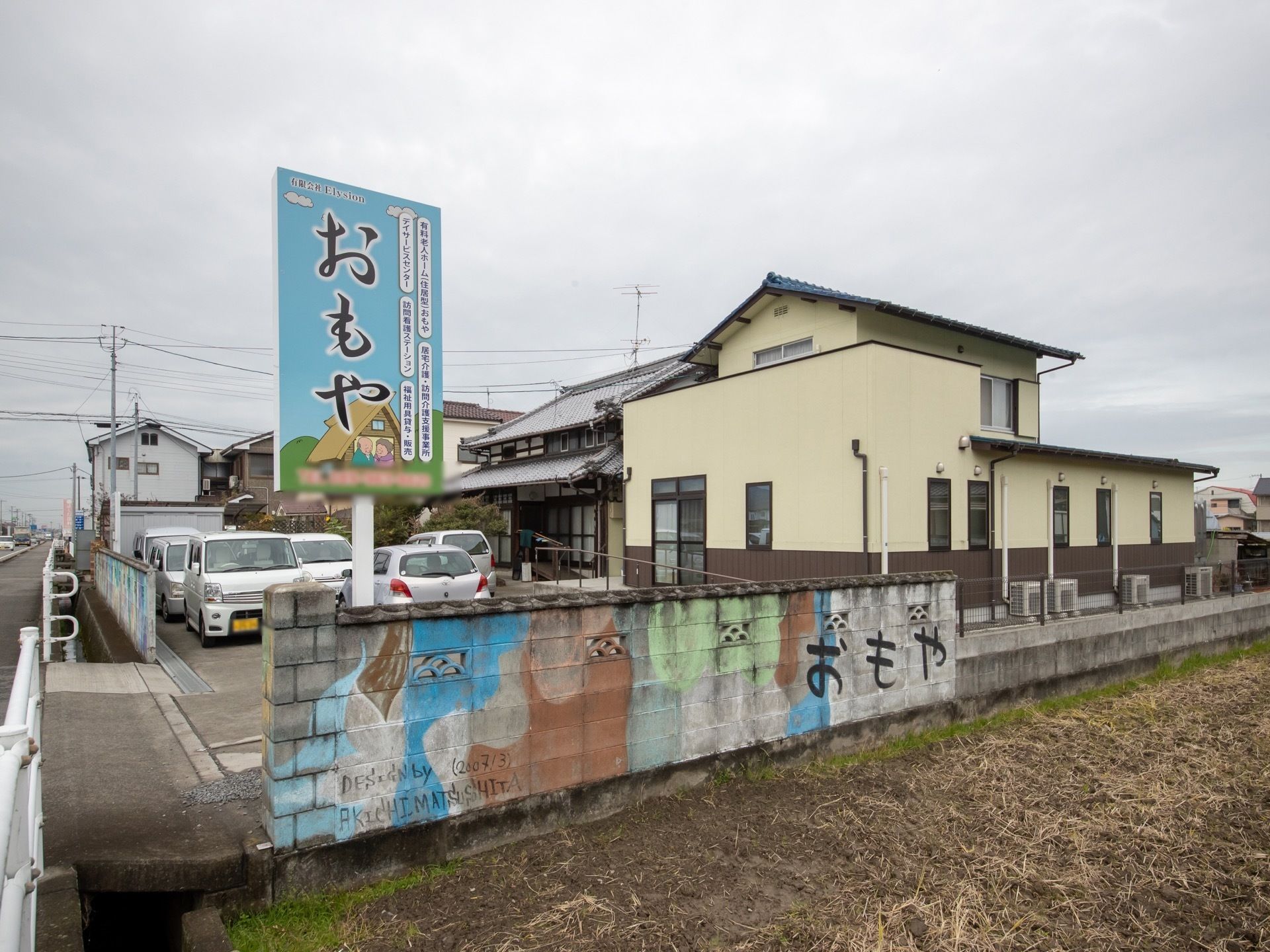 田んぼの横にあり、古民家と増築した建物が施設建物である。敷地の塀には、絵が描かれ、施設名を書いた看板も建てられている。