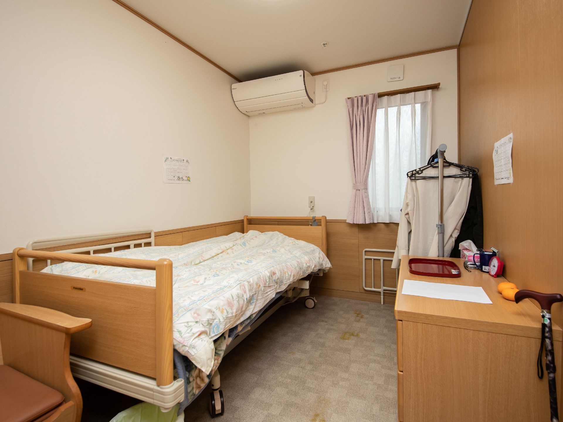 介護用ベッドには手すりがついていて寝起きするときにも安心。タンスや簡易トイレなどもあり、家庭で過ごすのと変わらない雰囲気で過ごせる。