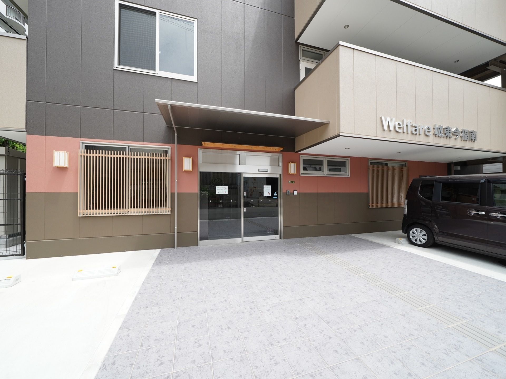 玄関前は屋根がせり出している。２階部分に施設名称が表示されている。施設前は駐車スペースになっている。