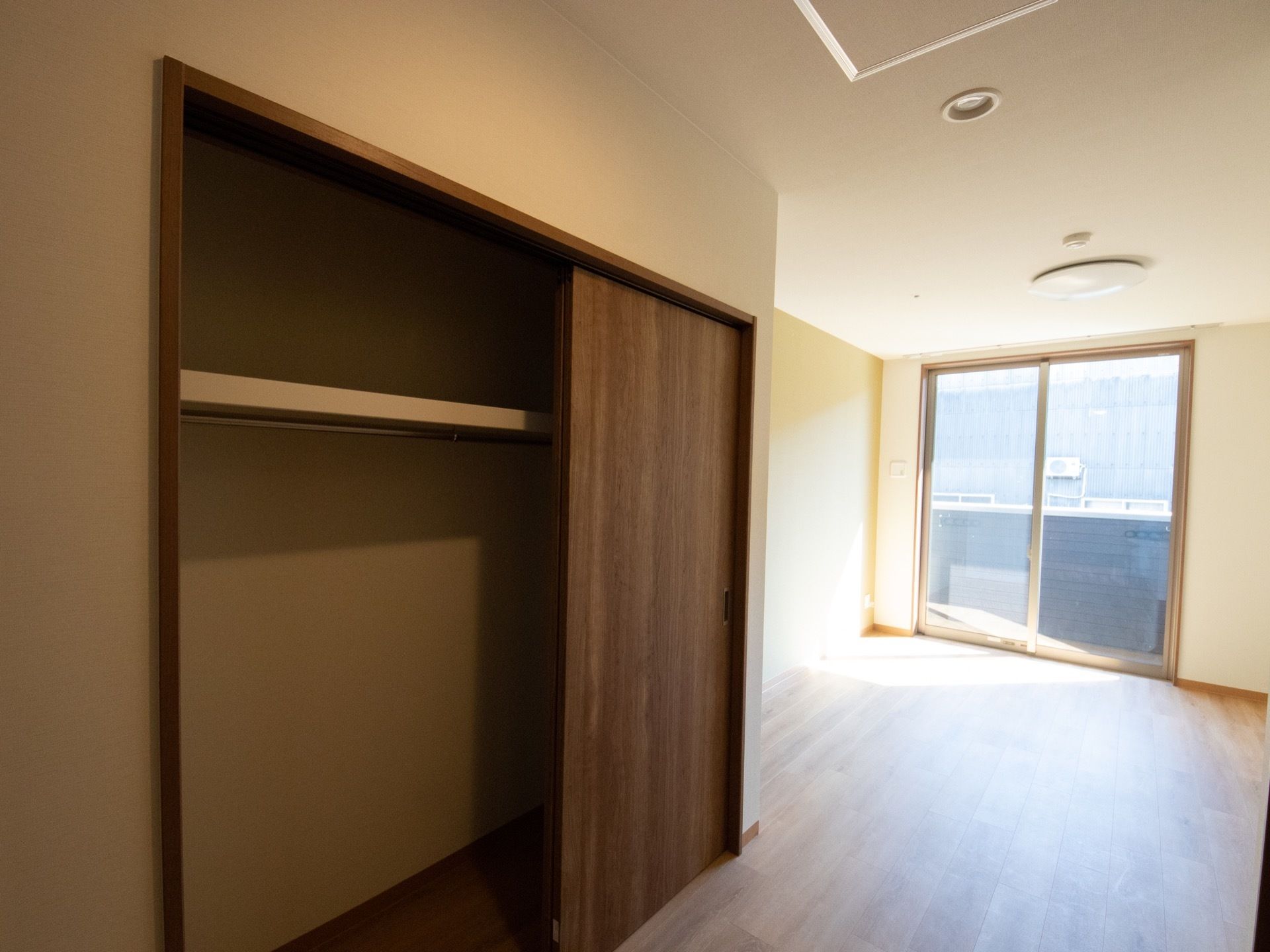 居室には大きな窓があり、そこから日が差し込んでいる。茶色い扉のクローゼットがある。上側に棚があり、2つのスペースに分かれている。