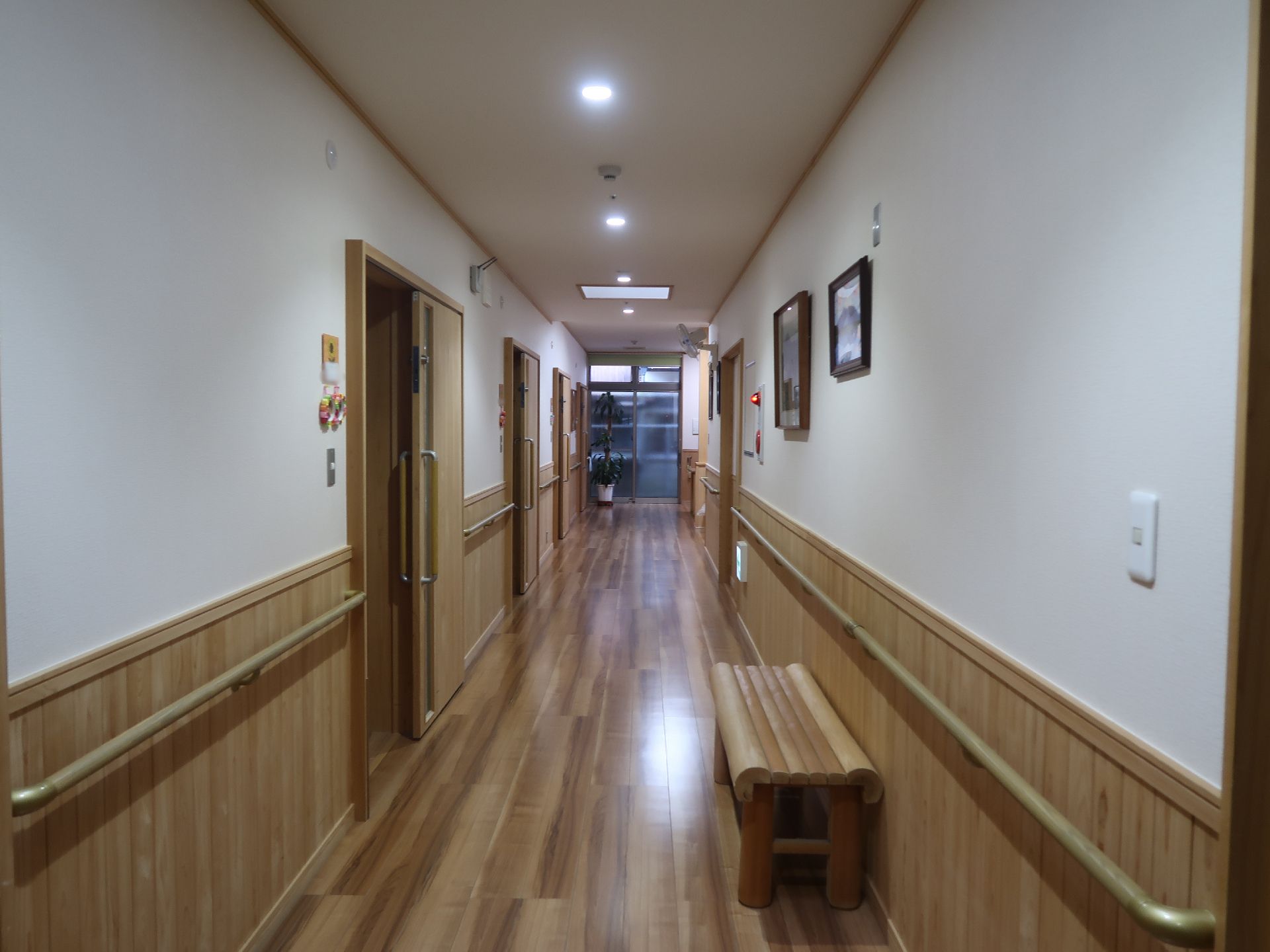 木の香りがしてくるような木材をふんだんに使用した館内。廊下はまっすぐで、両サイドに手すりと居室のドアが並んでいて、ベンチもある。